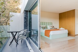 Ein modernes Schlafzimmer mit einem Bett, einer Glastür, die zu einem Balkon führt, und einem kleinen Tisch mit Stühlen.