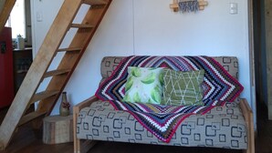A cozy loft bedroom with a wooden ladder, a patterned sofa, a colorful woven rug, and a small wall hanging. - Cabañas fundo tricahue (Talca)