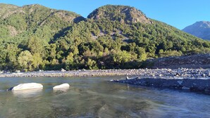 A river with clear water, surrounded by rocky banks and lush green hills. - Cabañas fundo tricahue (Talca)