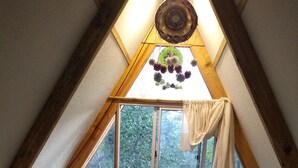 A cozy attic bedroom with a large window, a bed with a patterned blanket, and a hanging light fixture. - Cabañas fundo tricahue (Talca)