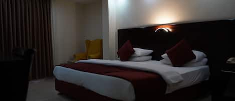 A hotel room with a bed, a chair, and a bedside table with a phone.