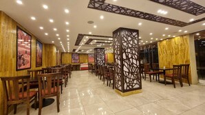 A spacious dining area with wooden chairs and tables, a decorative pillar, and ceiling lights. - Petra Agora Hotel (Wadi Musa)