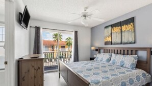 A bedroom with a bed, a ceiling fan, a TV mounted on the wall, and a balcony with a view of palm trees. - Beautiful Townhome at Lake Barkley With Pool View! (Kissimmee)
