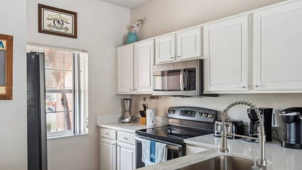 A modern kitchen with white cabinets, a stainless steel sink, a microwave, and a stove. - Beautiful Townhome at Lake Barkley With Pool View! (Kissimmee)