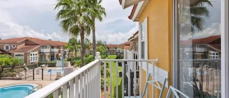Un balcon avec des balustrades blanches, une piscine et des palmiers en arrière-plan.