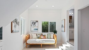Un interior modern amb un sofà llit, obra d'art emmarcada i una escala que condueix a una zona de cuina.