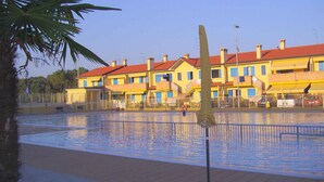 Une zone avec une piscine et un palmier, un bâtiment aux toits rouges, et une personne dans l’eau.
