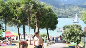 Een strandscène met palmbomen, mensen die ontspannen en een zeilboot op de achtergrond.