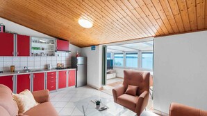 Una cocina moderna con armarios rojos, techo de madera y vistas al mar a través de amplios ventanales.