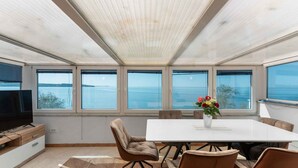 Una habitación moderna con una mesa grande, sillas cómodas, un televisor de pantalla plana y ventanas amplias que ofrecen vistas al mar.