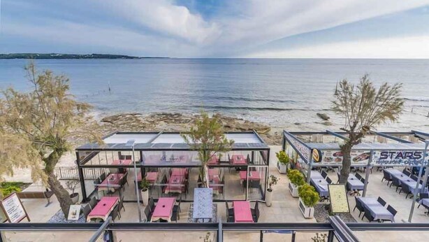 Un área de comedor al aire libre con mesas y sillas, con vista a una playa y al mar.