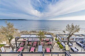 An outdoor dining area with tables and chairs, overlooking a beach and the sea. - Holiday apartment on the coast with sea view (Novigrad)