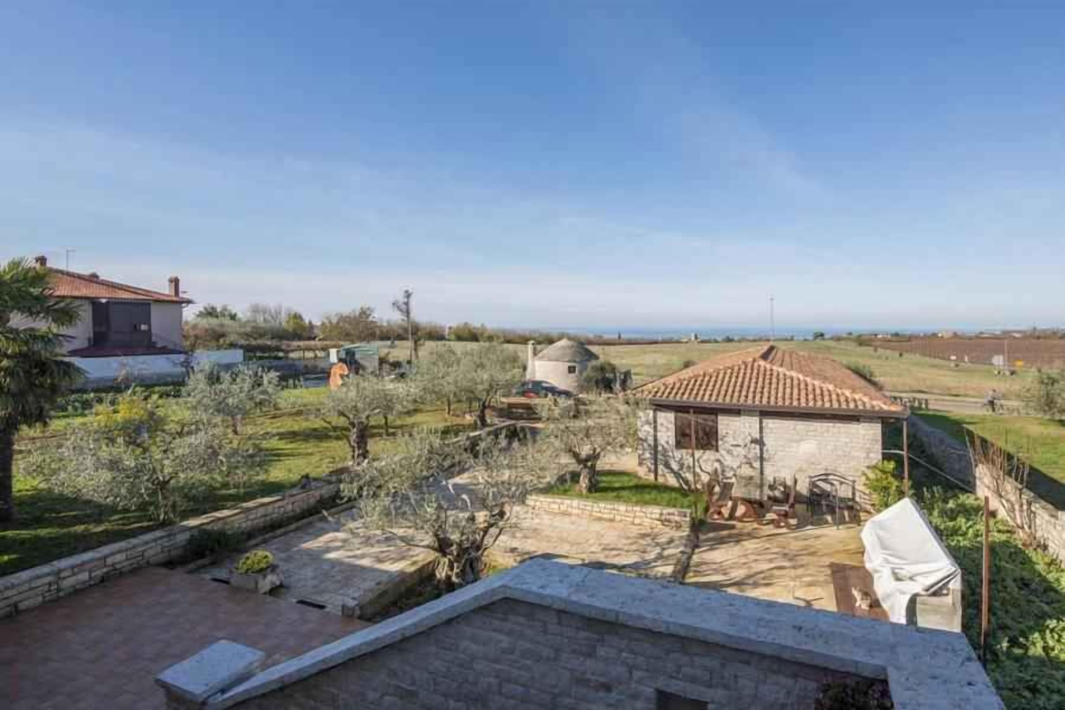 A rural property with a stone house, olive trees, and a clear sky.