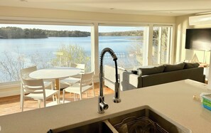 Une cuisine moderne dotée d’une grande fenêtre donnant sur un lac, un coin repas avec des chaises et un salon avec un canapé.