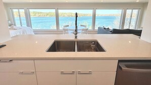 Een moderne keuken met een groot raam met uitzicht op een meer, een spoelbak en een eethoek met stoelen.