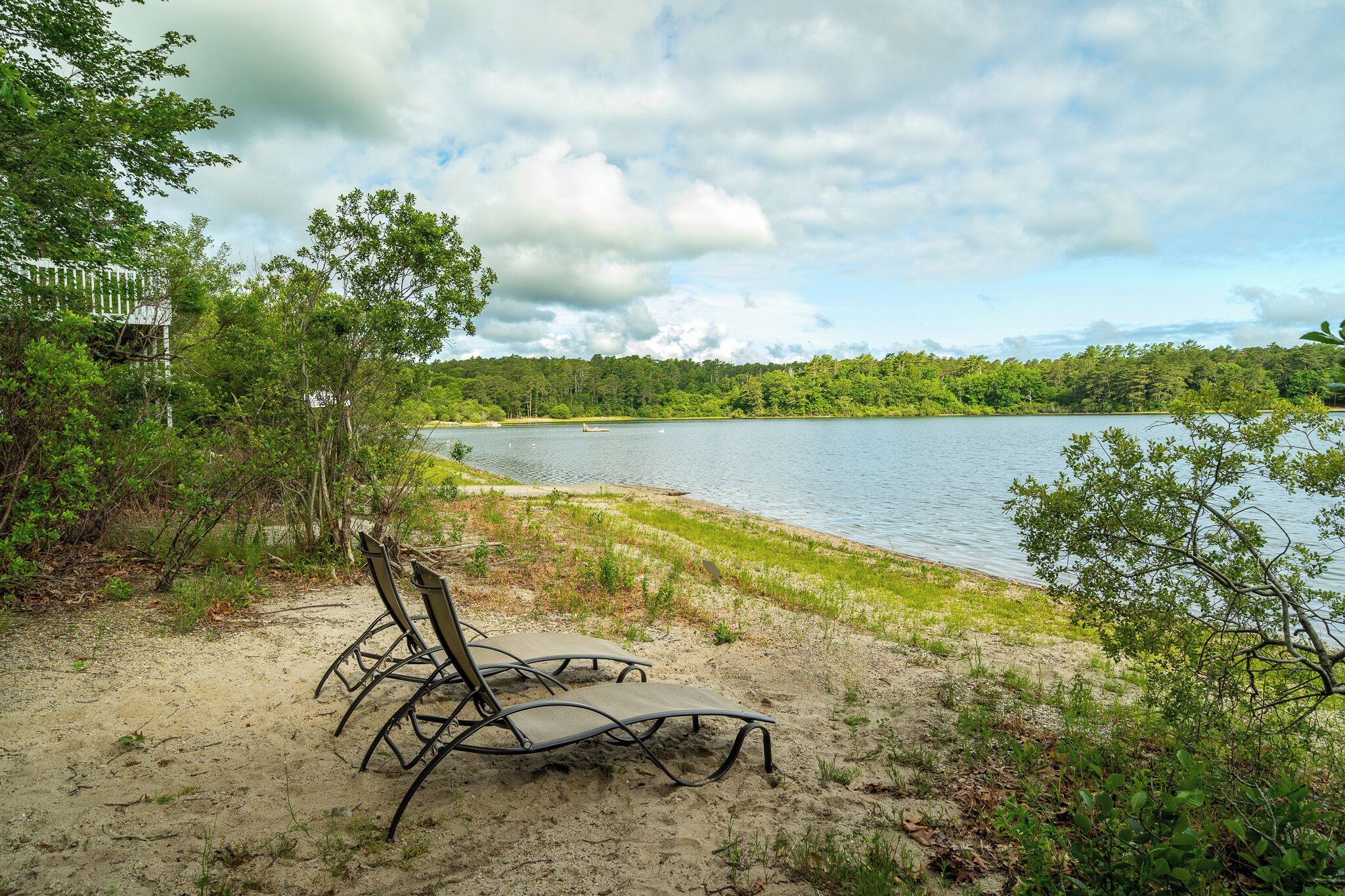 Une vue sur le lac, avec deux chaises longues sur le sable, entourées de verdure et sous un ciel nuageux.