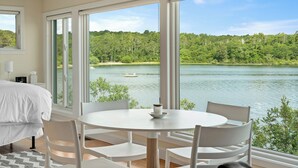Een slaapkamer met een groot raam met uitzicht op een meer en bos.