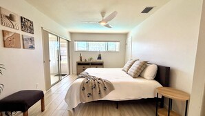 A bedroom with a bed, a bench, a dresser, a ceiling fan, and a window.