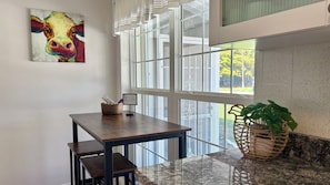 Una habitación con una mesa de comedor, sillas, un cuadro, una ventana con persianas y una planta.