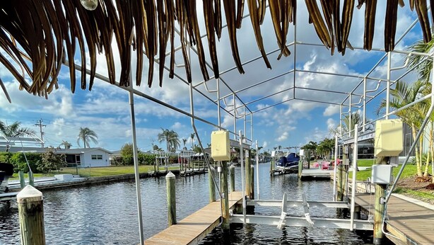 A wooden dock extending into calm water, with a thatched roof overhead.