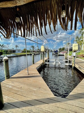 A wooden dock extending into calm water, with a thatched roof overhead.