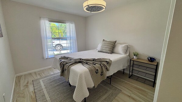 A bedroom with a bed, a window with curtains, a small table with a plant, and a radiator.