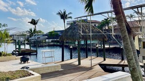A marina with boats docked, a thatched-roof structure, and a grassy area with steps leading to a dock.