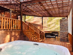 A wooden deck with a hot tub, wooden railings, and a stone wall.