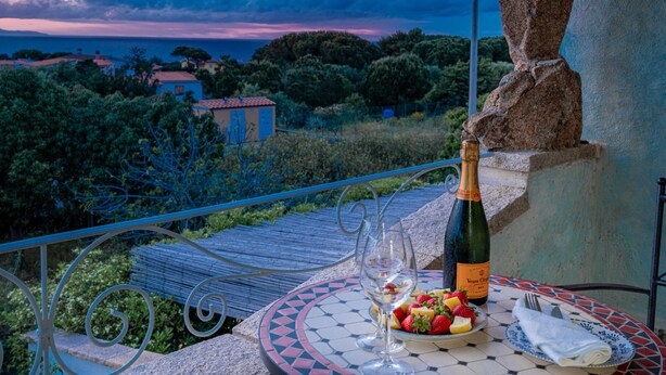 A table with a bottle of Veuve Clicquot champagne, a glass, and a plate of strawberries and cheese on a balcony overlooking a scenic view.