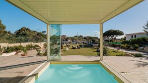 A swimming pool with a glass enclosure, surrounded by a garden and a view of a residential area.