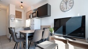 Une cuisine moderne avec un coin repas, un téléviseur à écran plat et une grande horloge murale.