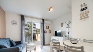 Un salon moderne comprenant un canapé, une table à manger, des chaises, un téléviseur et un balcon avec des rideaux.