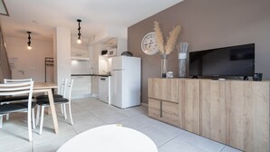 A modern kitchen with white appliances, a dining area with a white table and chairs, and a TV on a wooden cabinet. - Villa duplex 6 pers with garden and air conditioning (Sérignan)