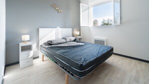 Une chambre à coucher moderne avec un lit, des tables de chevet, une fenêtre et un radiateur.