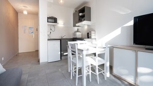 A modern kitchen with white appliances, a dining area with white chairs, and a flat-screen TV on a wooden stand. - Bright villa 4 ppl, garden, close to the sea (Sérignan)