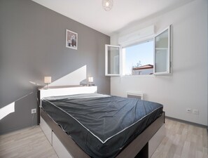 Une chambre à coucher moderne avec un lit, des lampes de chevet, une fenêtre et un petit tableau accroché au mur.