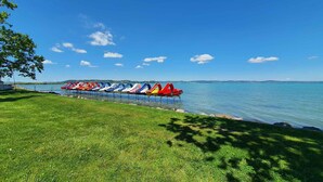 Eine Reihe bunter Tretboote auf einem ruhigen See, im Vordergrund eine Rasenfläche und ein klarer, blauer Himmel.