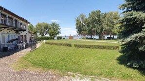 A two-story building with a balcony, a covered entrance, and a paved driveway. - Holiday apartment directly on the water with free beach (Zamárdi)