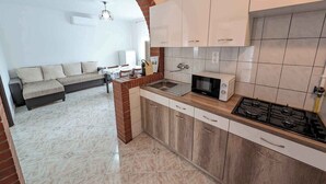Eine kompakte Küche mit Gasherd, Mikrowelle und Spüle. Es gibt einen Essbereich mit einer Couch und einem Tisch. Die Küche verfügt über ein Ziegelbogenportal und weiße Schränke.