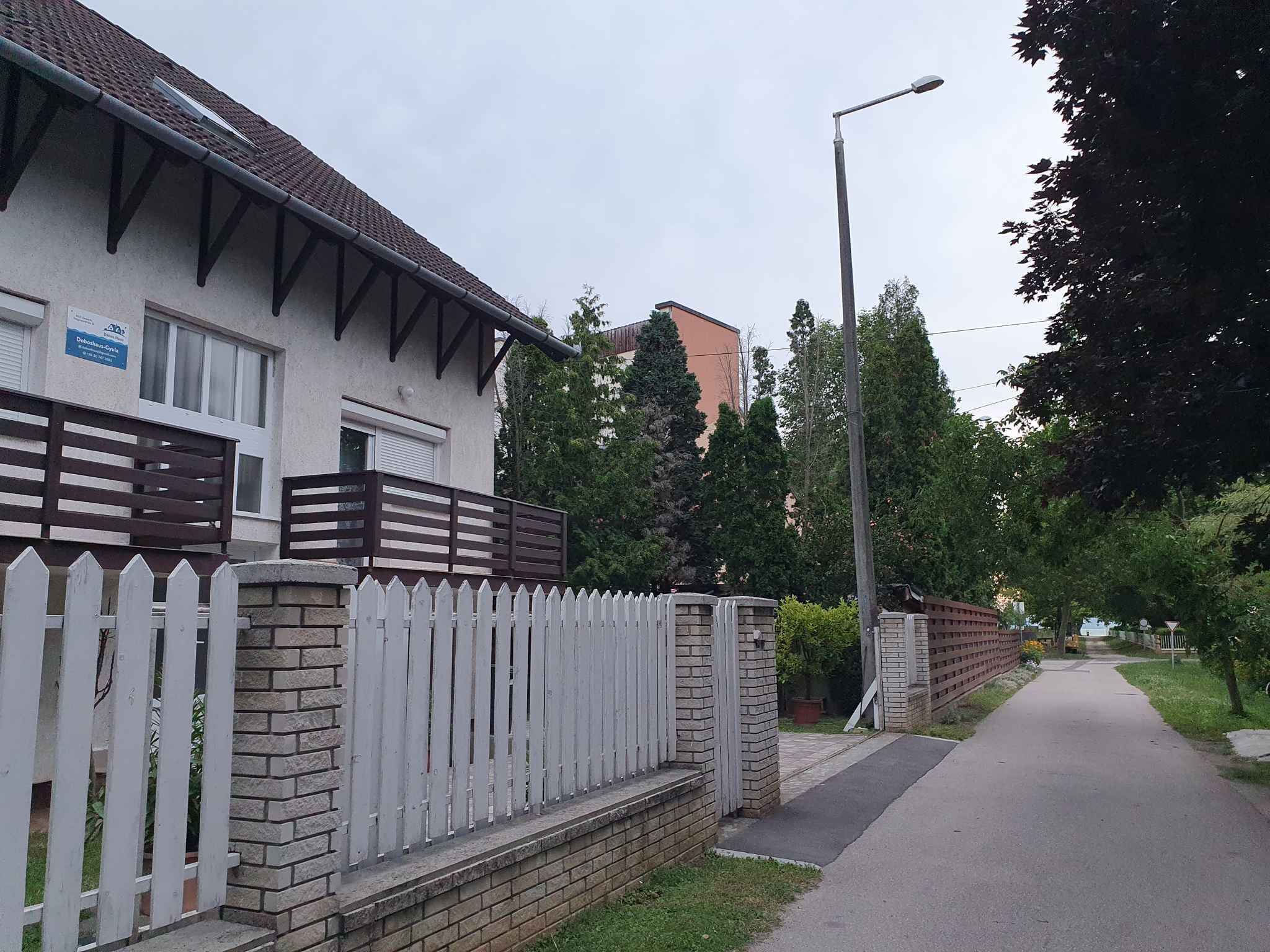 A residential street with a white picket fence, a brick wall, and a paved sidewalk.