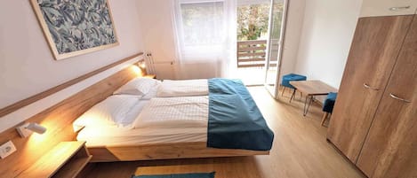 A bedroom with a bed, bedside table, lamp, wardrobe, and a view of the outside.