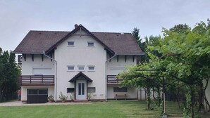 A two-story house with a flat roof, a front porch, and a small garden area. - Holiday apartment near the water with WLAN and air conditioning (Zamárdi)