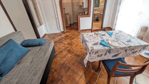 A dining area with a table set for two, a sofa with blue cushions, and a kitchen visible through an archway. - Holiday apartment near the water with WLAN and air conditioning (Zamárdi)