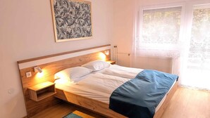 A single bed with a wooden headboard, bedside lamps, a blue blanket, and a framed artwork above. - Holiday apartment near the water with WLAN and air conditioning (Zamárdi)