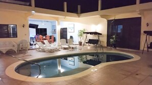 En indendørs swimmingpool med buet kant, omgivet af liggestole og et spiseområde.