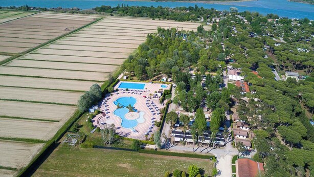 An aerial view of a resort with a central pool area, surrounding greenery, and adjacent fields. - Mobile home with air conditioning, terrace and pool (Caorle)