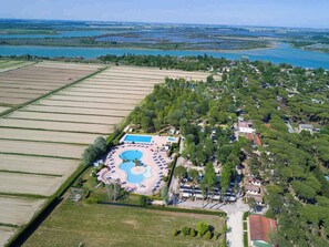Vue aérienne d’un complexe hôtelier doté d’une piscine centrale, entouré de verdure et bordé de champs.