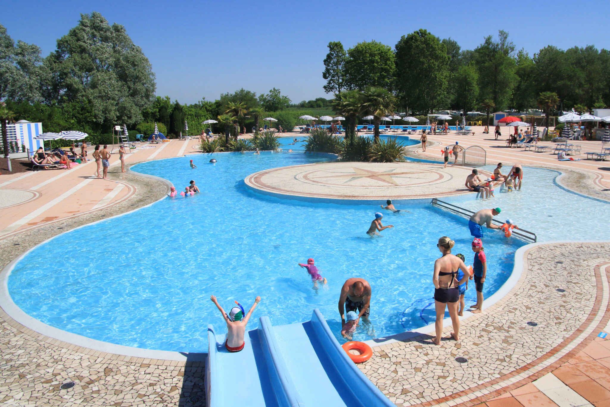 Una grande piscina all'aperto con uno scivolo, circondata da lettini e ombrelloni.