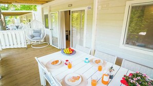 A covered outdoor dining area with a table set for breakfast, including croissants and fruit. - Mobile home with air conditioning, terrace and pool (Caorle)