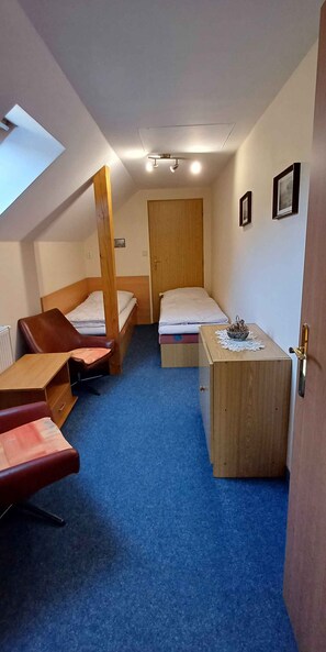 A compact room with two single beds, a wooden desk, a chair, and a small table with a decorative item.